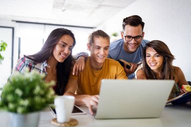 Four colleagues gathered around a laptop, collaborating in an open work environment